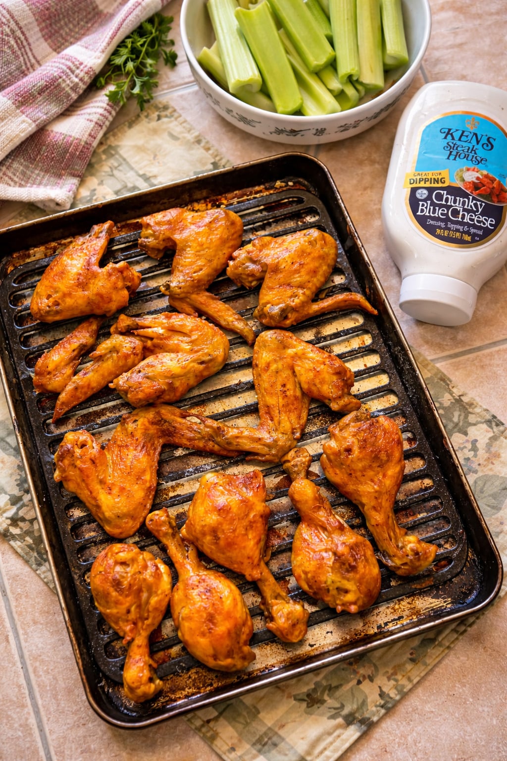 Crispy baked chicken wings on a black tray served with fresh celery sticks and chunky blue cheese dressing, styled on a rustic kitchen counter for a homemade appetizer.