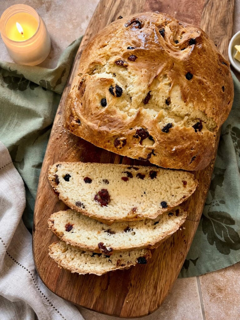 Homemade Irish soda bread loaf with traditional cross on top, sliced and served on wooden board with rustic kitchen styling.