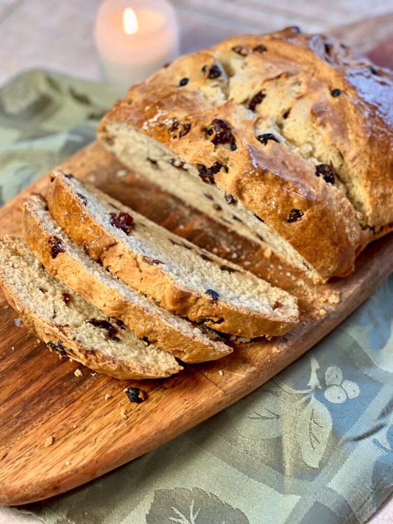 Freshly baked Irish soda bread with dried fruit sliced on rustic wooden board, golden brown crust and soft interior.