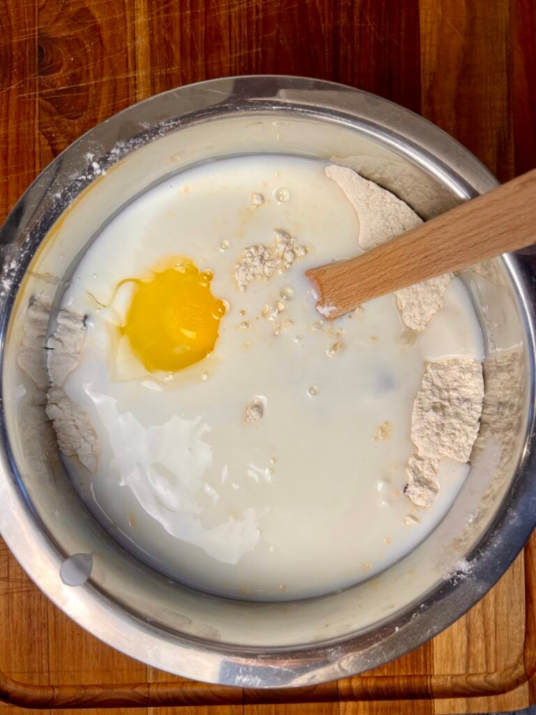 Buttermilk and eggs added to flour mixture for Irish soda bread recipe in stainless steel mixing bowl.