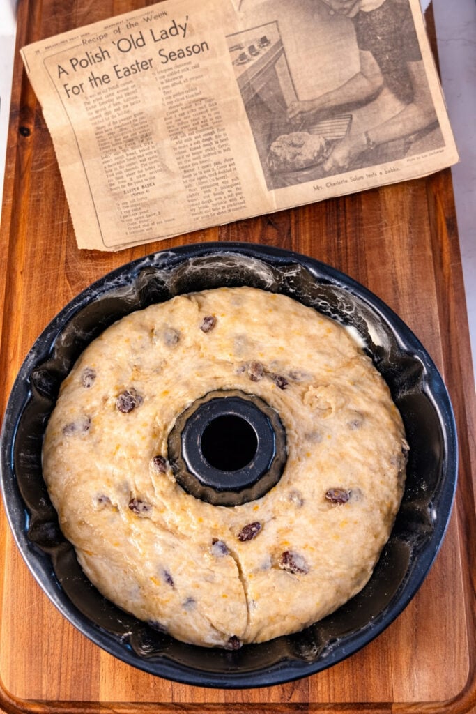 Traditional babka dough rising in a greased Bundt pan with raisins and orange zest, vintage Polish babka bread recipe inspiration