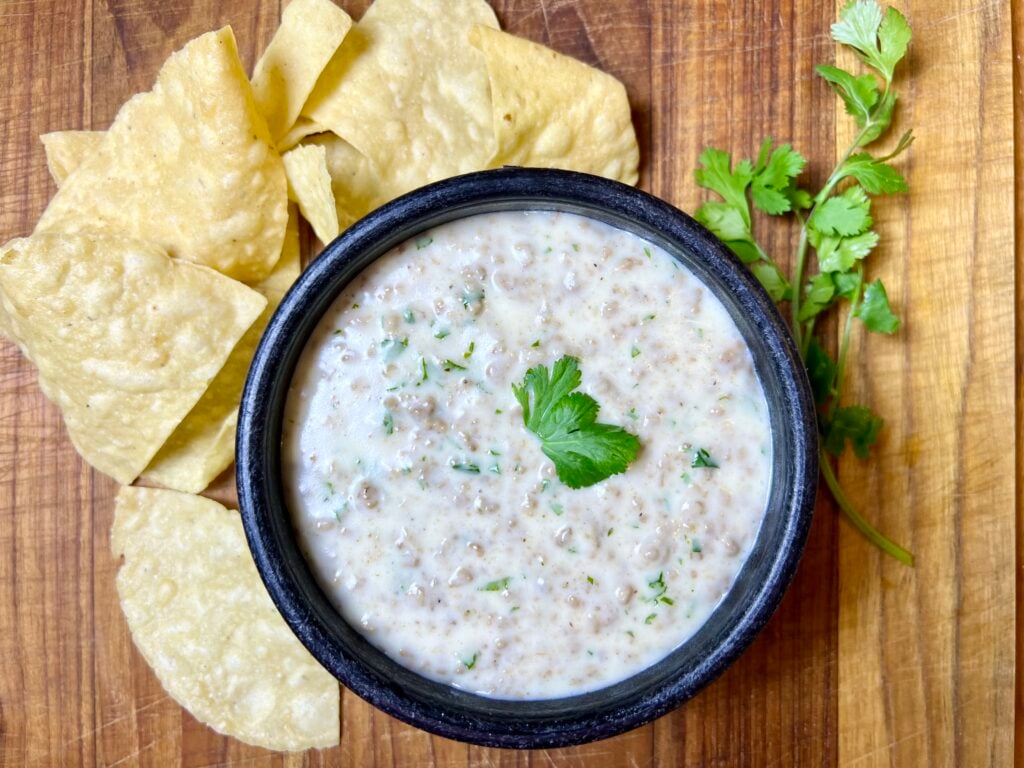 Creamy homemade queso dip with ground beef served with tortilla chips and fresh cilantro garnish.
