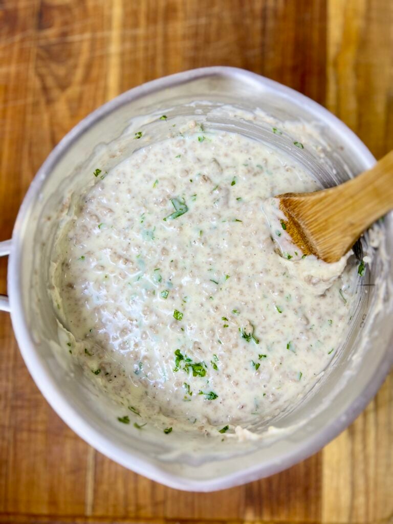 Creamy white queso dip with ground beef and chopped cilantro being stirred in a saucepan.