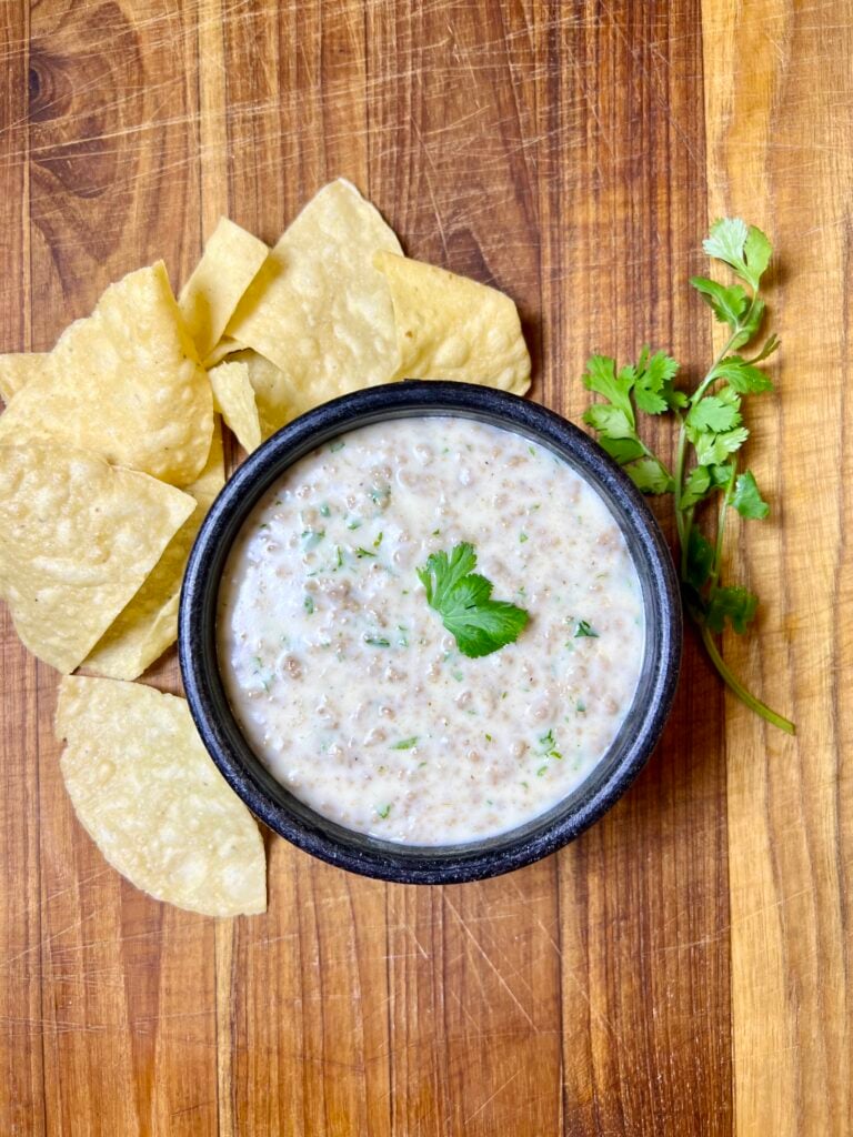 Creamy homemade queso dip with ground beef served with tortilla chips and fresh cilantro garnish.