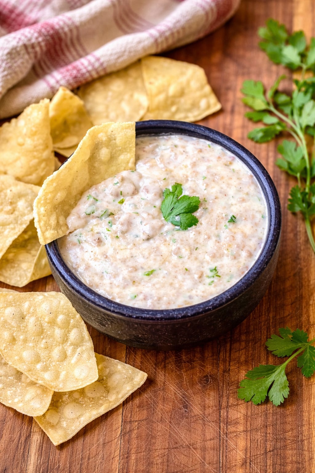 Homemade queso dip with ground beef in a bowl on a wooden board with tortilla chips and fresh cilantro.