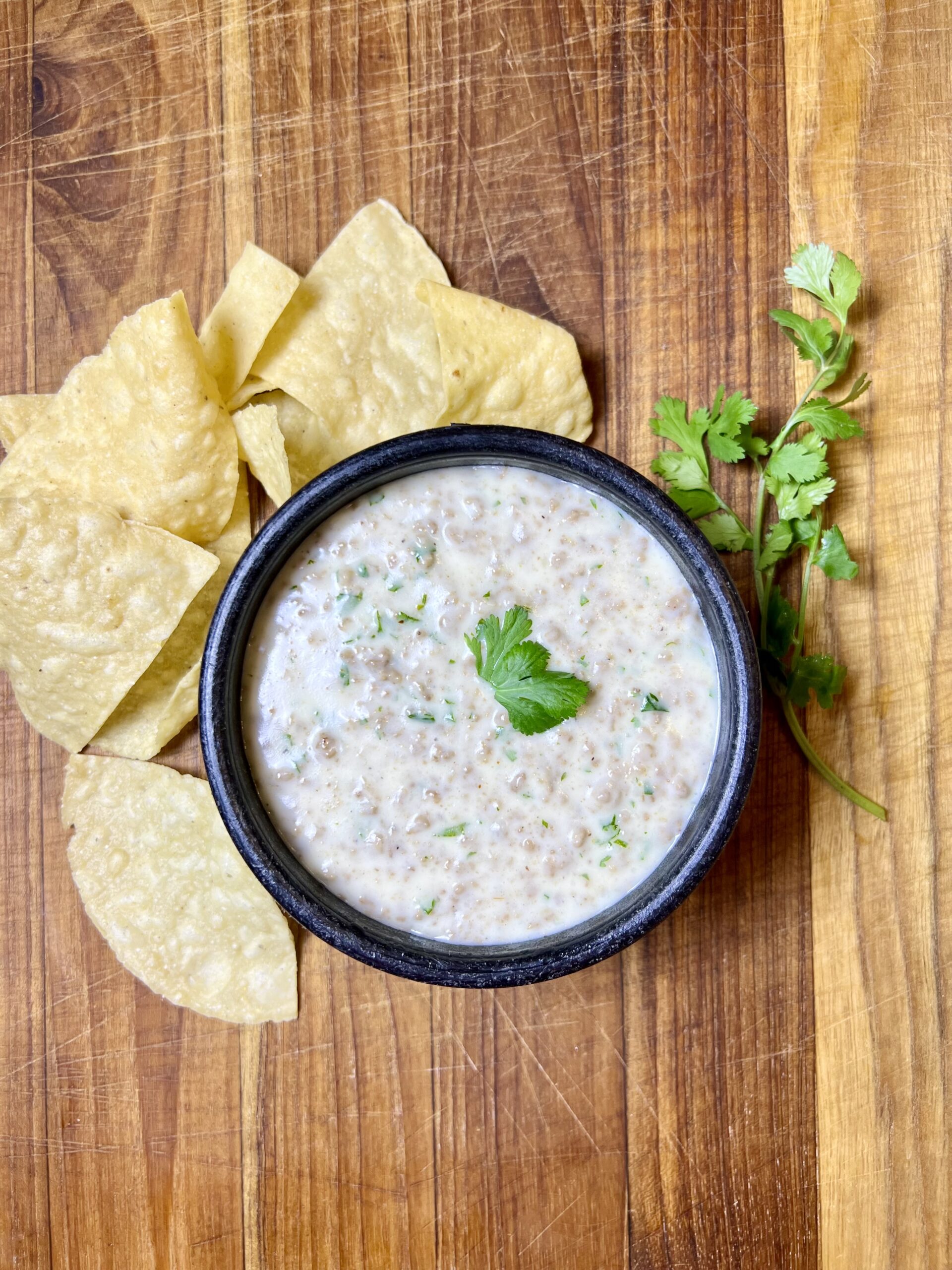 Creamy homemade queso dip with ground beef served with tortilla chips and fresh cilantro garnish.
