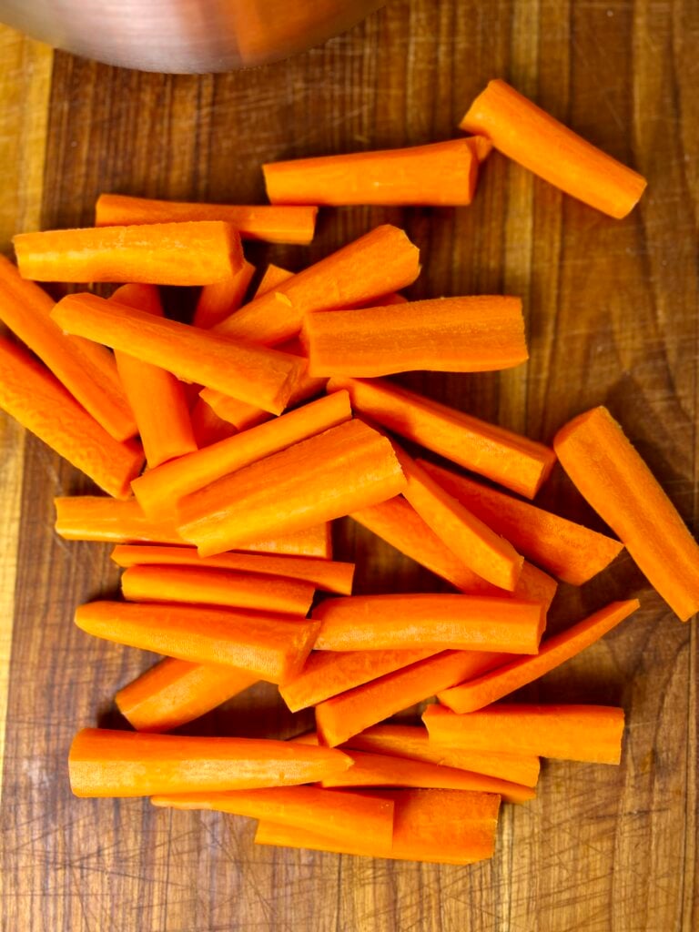 Freshly cut carrot sticks on wooden cutting board for homemade slow cooker glazed carrots.