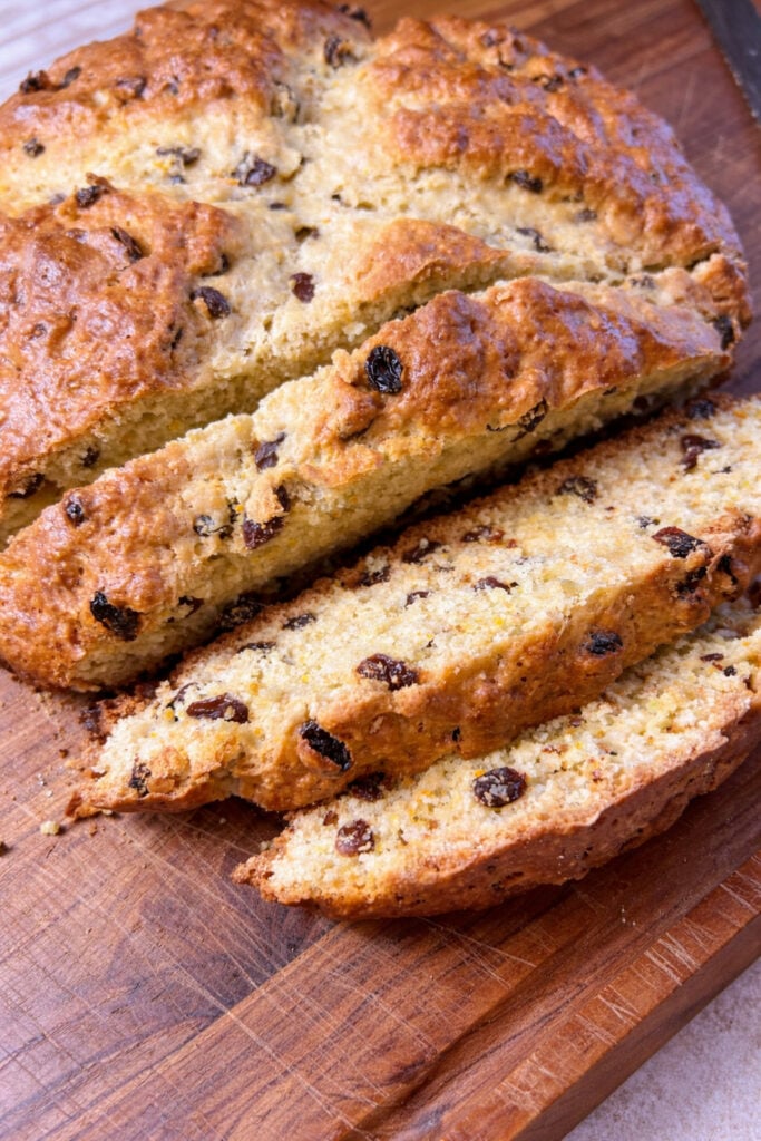 sourdough Irish soda bread recipe sliced on wooden cutting board with raisins and golden brown crust