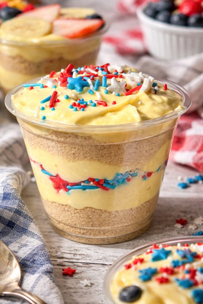 Close up of easy 4th of July vanilla dirt cups layered with Golden Oreo crumbs, creamy pudding, and patriotic red white and blue sprinkles in clear cup