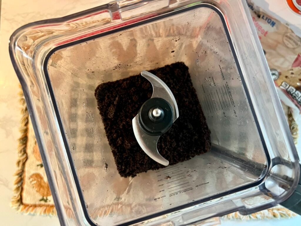 Crushing Oreo cookies into fine crumbs in a food processor for worms in dirt dessert recipe to create realistic dirt texture for dirt cake cups