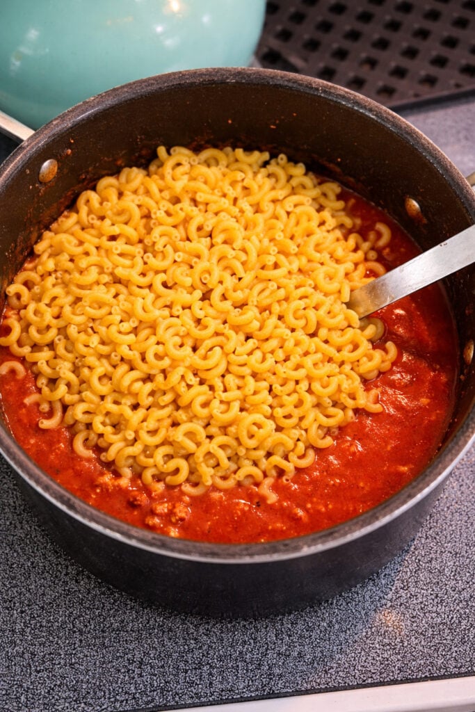 American chop suey recipe beef with elbow macaroni noodles added to tomato beef sauce in a pot, cooking pasta directly in the sauce