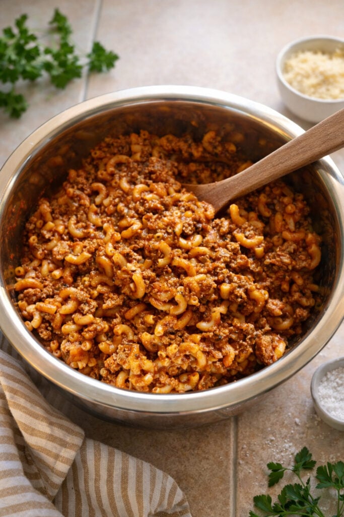 American chop suey recipe beef served in a metal bowl with elbow macaroni noodles, ground beef, and rich tomato sauce, topped with parmesan cheese