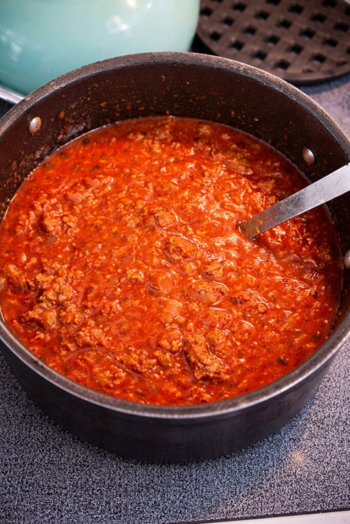 American chop suey recipe beef sauce simmering in a pot with ground beef, tomato sauce, garlic, and Italian seasoning over medium heat