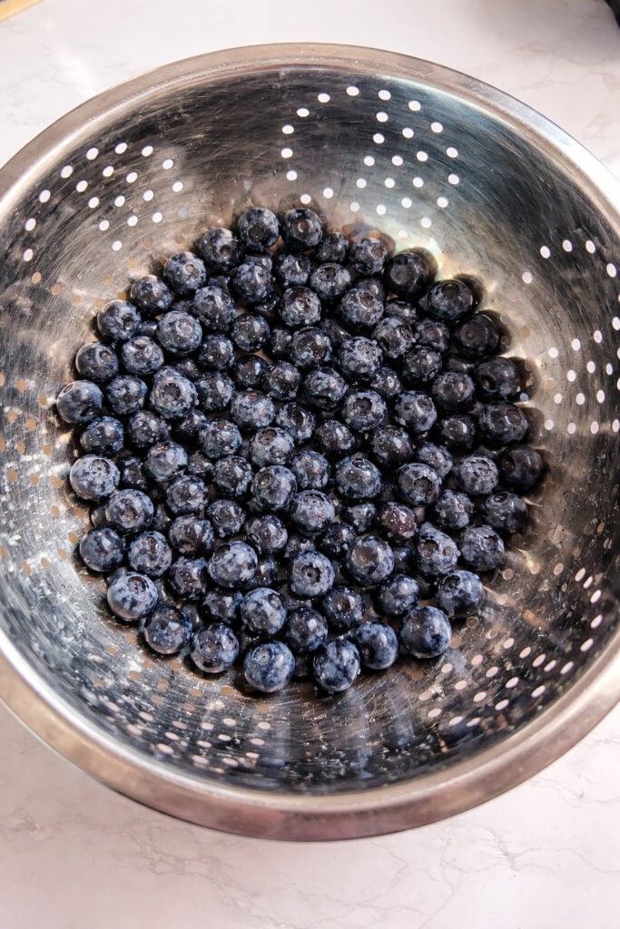 Blueberries strained in a colander, ready to create a smooth, vibrant blue layer for delicious, homemade popsicles.