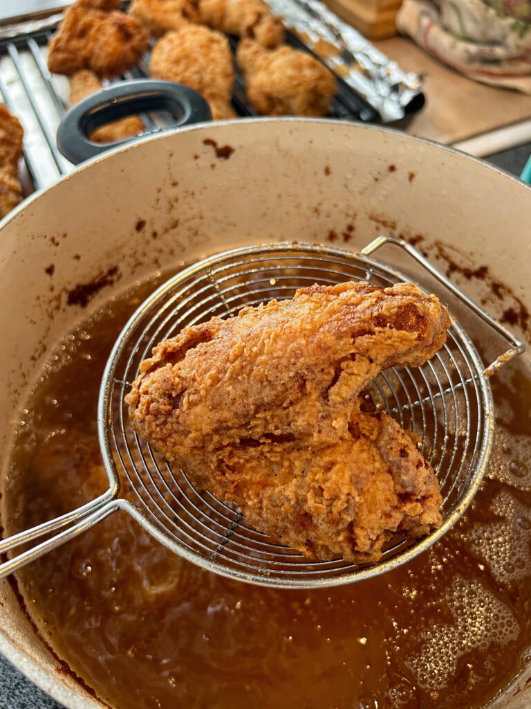 Fried chicken lifted from hot oil showing crispy coating in Bojangles chicken recipe