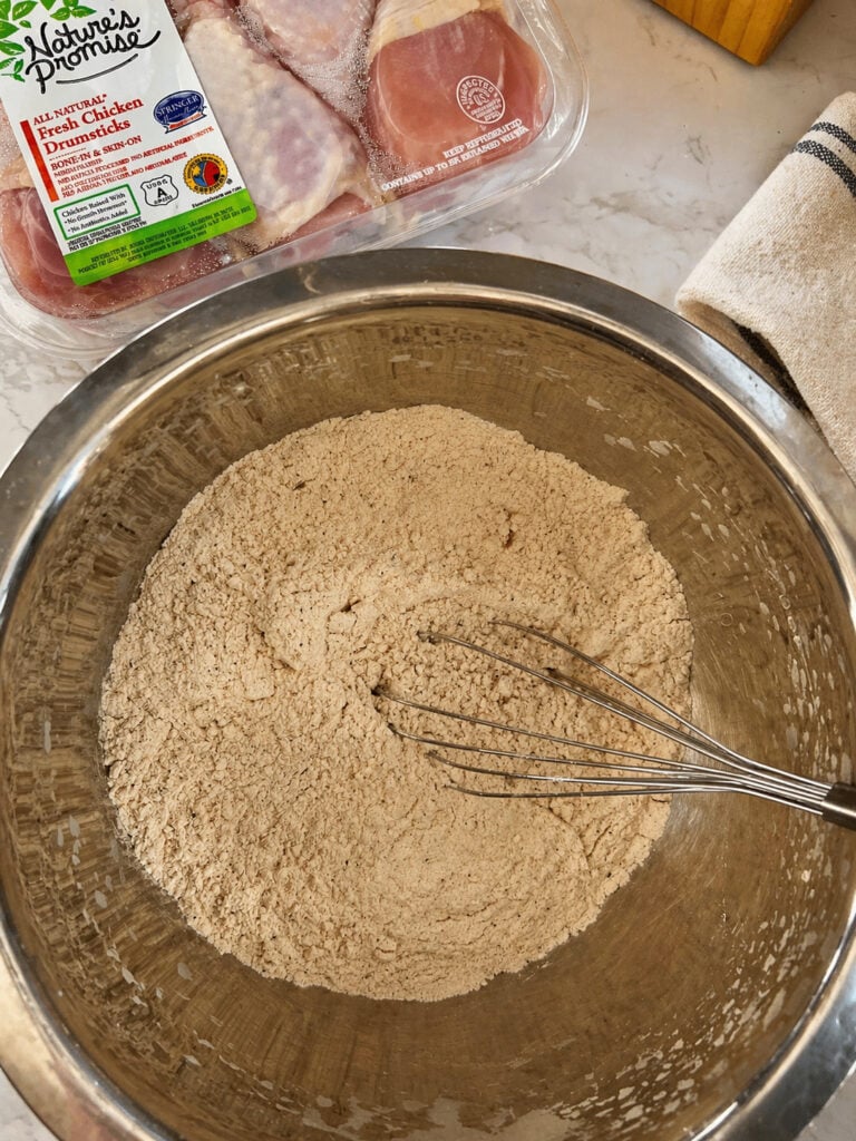 Seasoned flour mixture in large bowl with raw chicken for Bojangles chicken recipe preparation