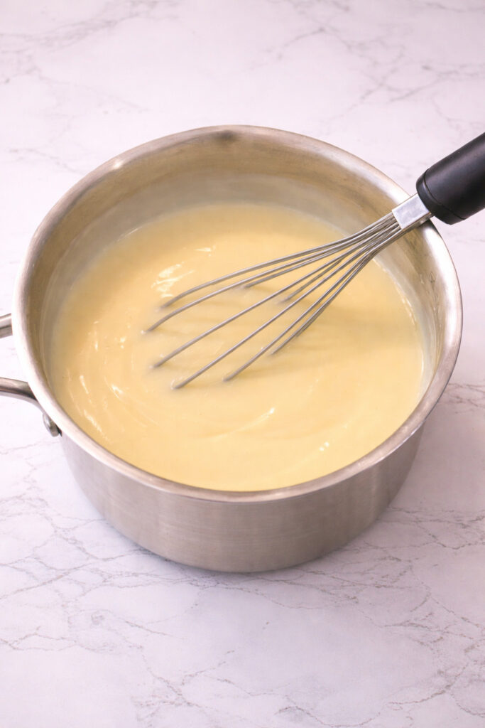 Homemade vanilla pudding cooking in a saucepan with a whisk, smooth and creamy texture, easy from-scratch vanilla pudding recipe