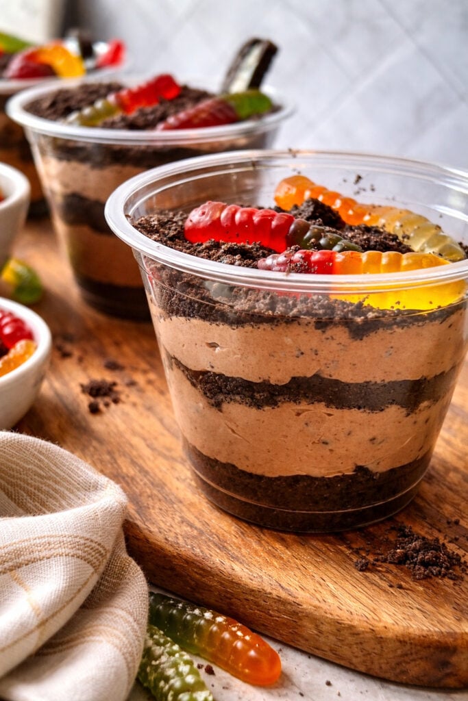 Worms in dirt dessert recipe served in clear plastic cups with layers of chocolate pudding and Oreo crumbs topped with gummy worms for a fun party dessert