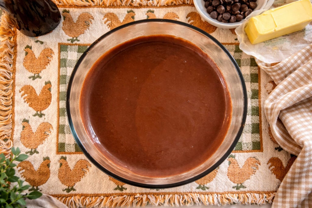 Top view of homemade chocolate pudding in a glass bowl, showing a rich, glossy surface and smooth consistency on a rustic farmhouse kitchen towel