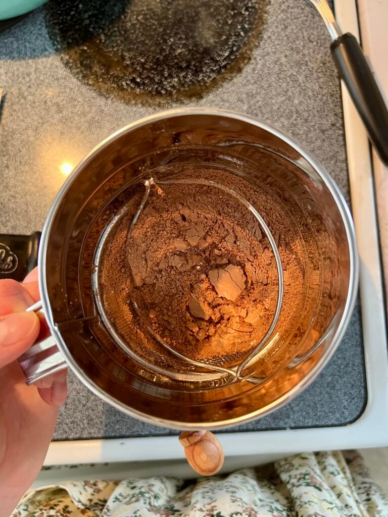 Sifting cocoa powder and dry ingredients for homemade chocolate pudding using a fine mesh strainer to remove lumps for a smooth texture