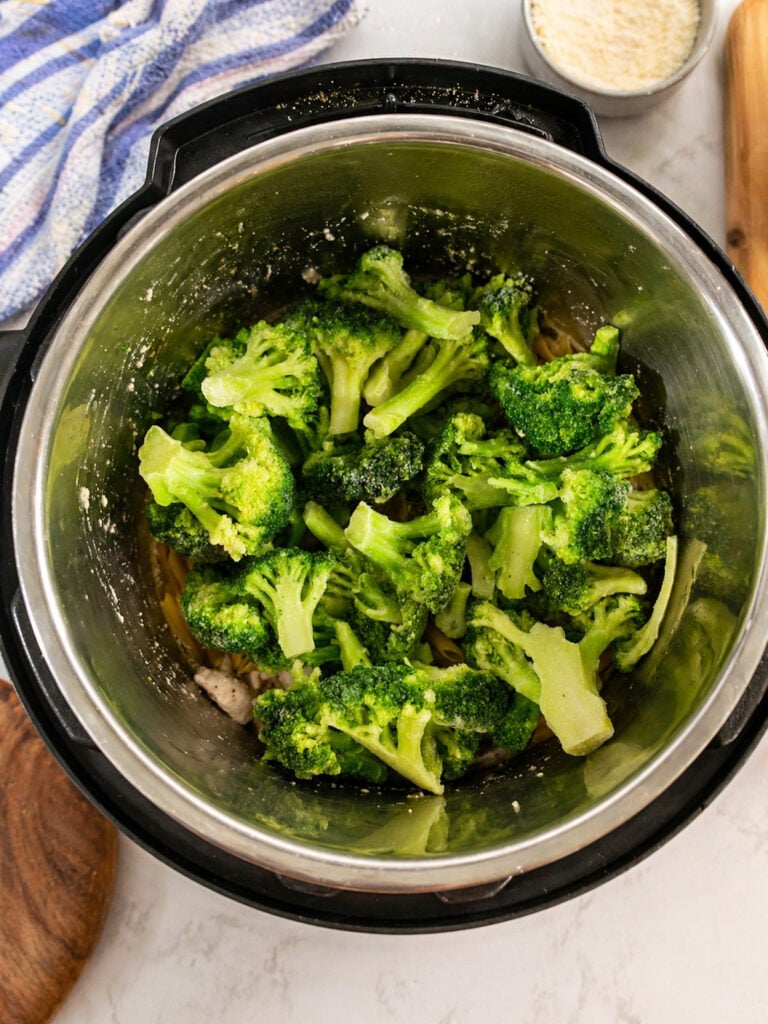 Fresh broccoli added to Instant Pot chicken broccoli pasta during cooking process
