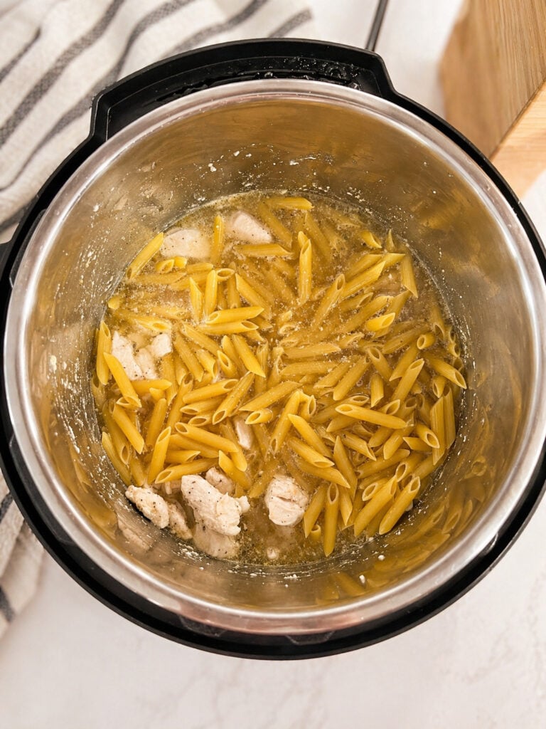 Uncooked penne pasta and chicken in broth inside Instant Pot for chicken broccoli pasta
