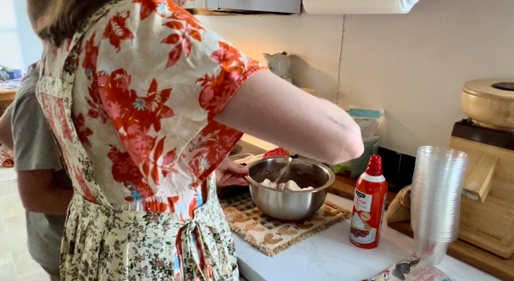 Making worms in dirt dessert recipe by mixing creamy chocolate pudding and whipped topping in a bowl, step by step easy no bake dirt cake tutorial