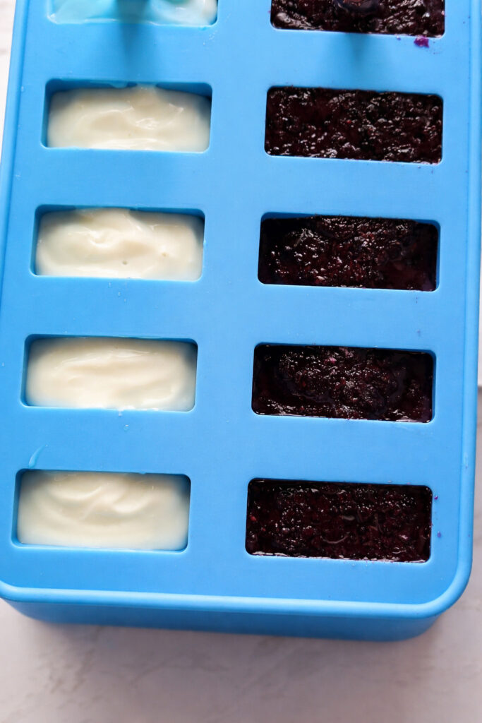 Layered red, white, and blue popsicles, vibrant and ready for a cool summer treat, neatly arranged in a silicone mold, awaiting the freezing process to create delicious, patriotic perfection.