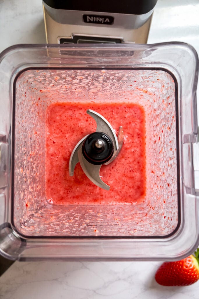 Top view inside a blender showing freshly blended strawberry mixture for popsicle base