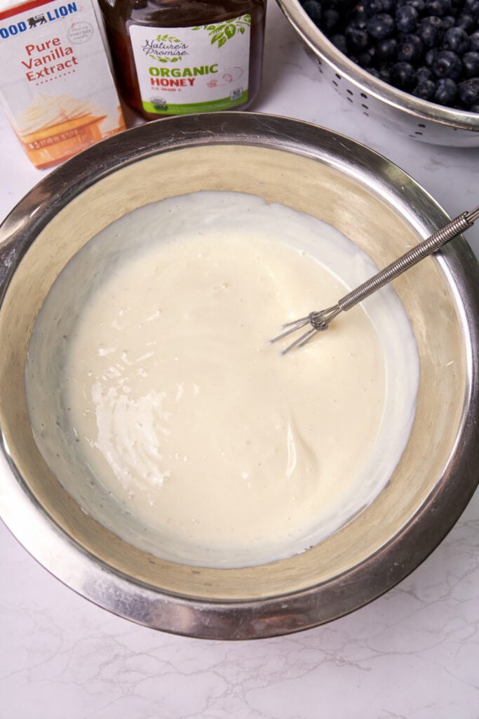 Yogurt mixture on a stainless steel bowl with a whisk. 