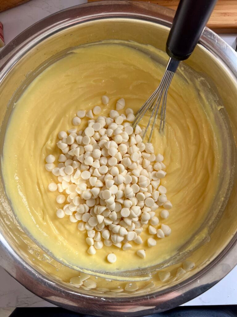 White chocolate chips being added to creamy vanilla pudding mixture in a large bowl for easy 4th of July vanilla dirt cups, showing smooth texture and step-by-step no bake dessert preparation