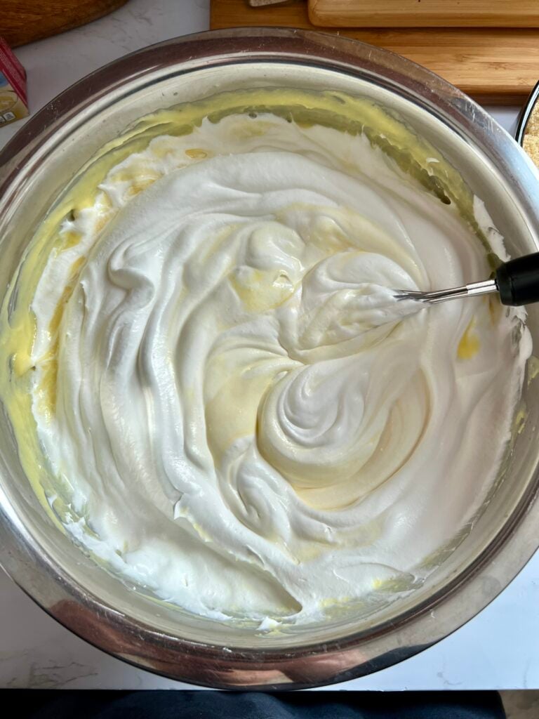 Whipped topping being folded into vanilla pudding mixture to create light fluffy texture for easy 4th of July vanilla dirt cups
