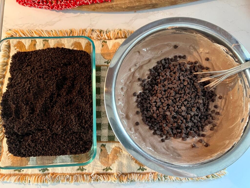 Creamy chocolate pudding mixture with mini chocolate chips next to crushed Oreo cookie crumbs for layering worms in dirt dessert recipe