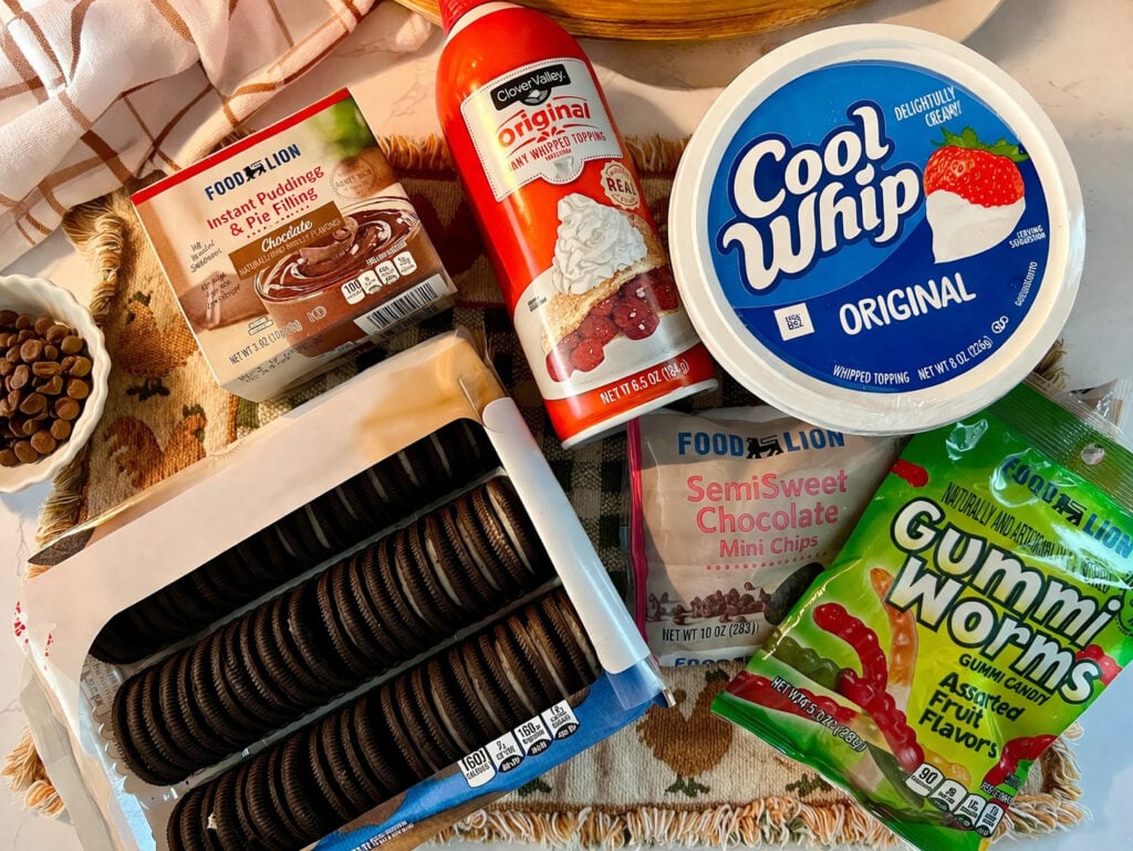 Ingredients for worms in dirt dessert recipe including Oreo cookies, instant chocolate pudding mix, Cool Whip, mini chocolate chips, and gummy worms