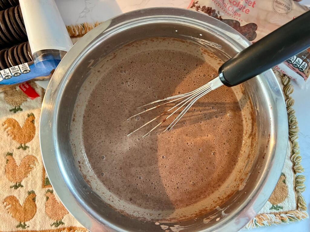 Mixing instant chocolate pudding with milk in a bowl for worms in dirt dessert recipe, showing early stage of creamy pudding mixture before thickening