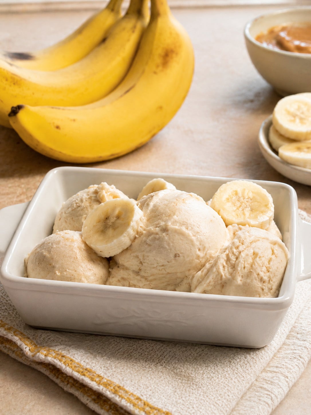 Homemade 3 ingredient banana ice cream scooped into a white serving dish and topped with fresh banana slices. This easy no-churn banana ice cream recipe is made with ripe bananas, heavy cream, and brown sugar for a creamy frozen dessert.