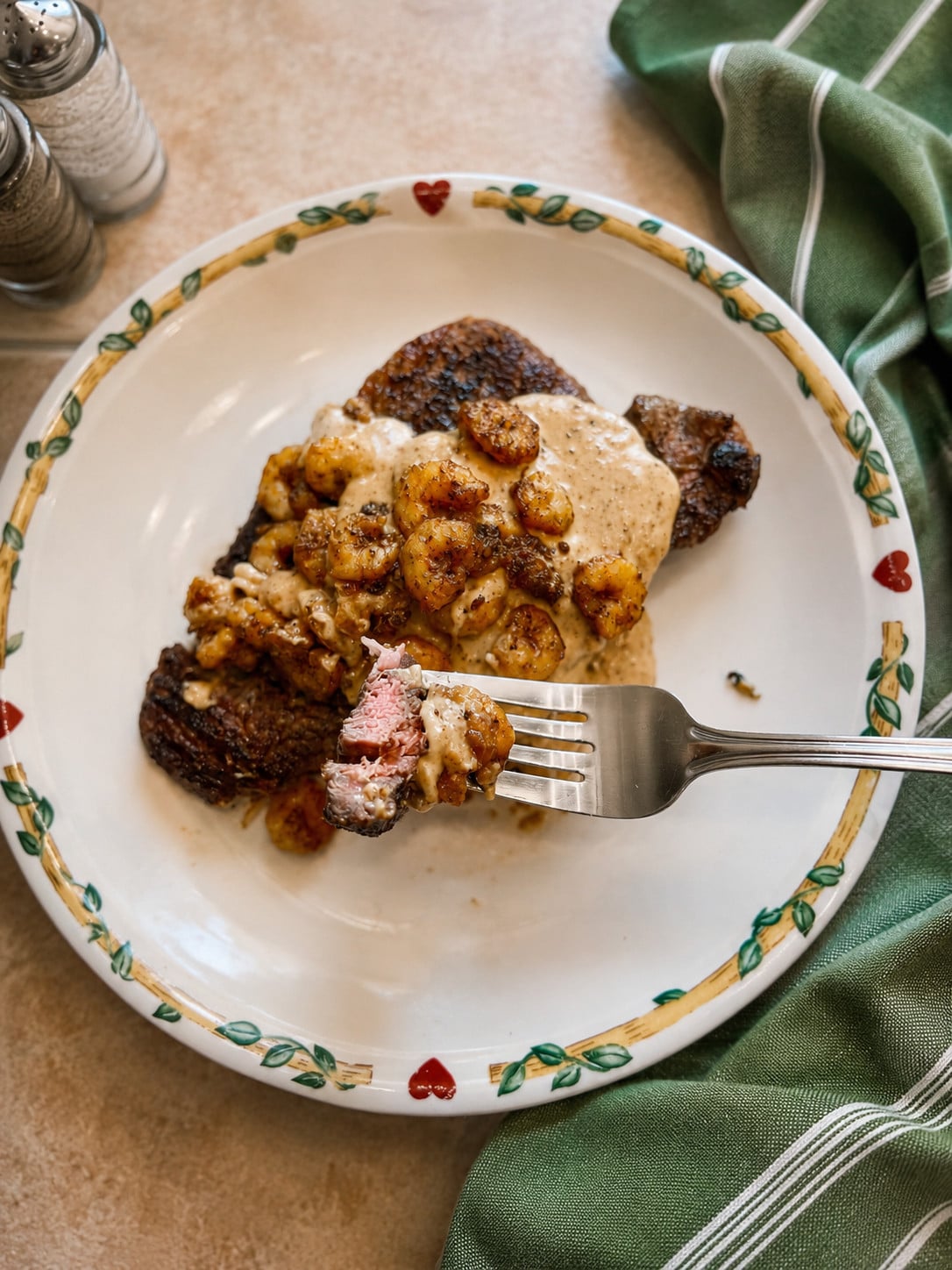 Fork holding a bite of juicy steak topped with parmesan cream sauce and seasoned shrimp in a copycat Applebee’s parmesan steak and shrimp recipe.