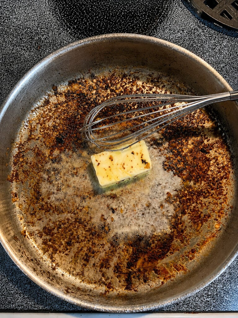 Butter melting in a skillet with browned bits to make creamy parmesan sauce for steak and shrimp.