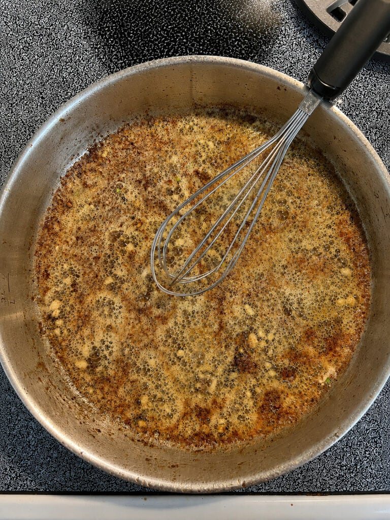 Creamy parmesan sauce simmering in a skillet for Applebee’s inspired steak and shrimp.