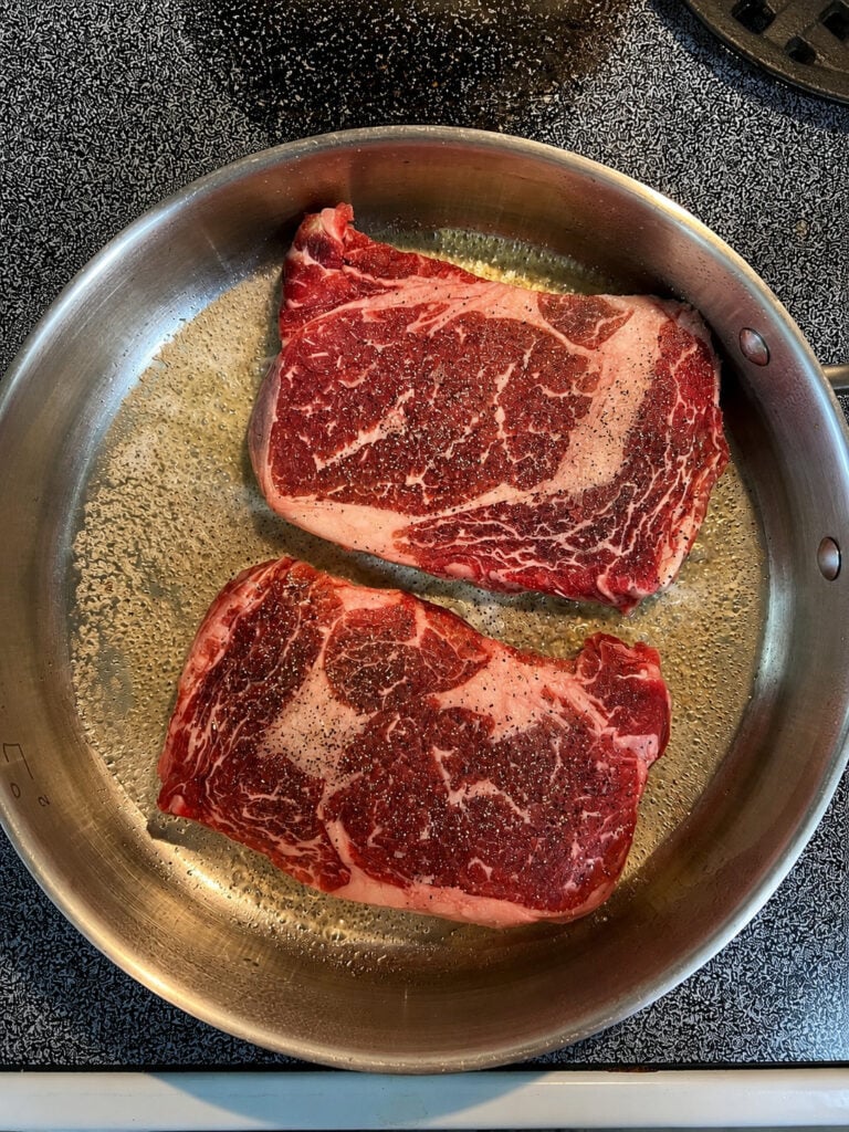 Ribeye steaks cooking in a skillet for a homemade Applebee’s parmesan steak and shrimp copycat dinner.