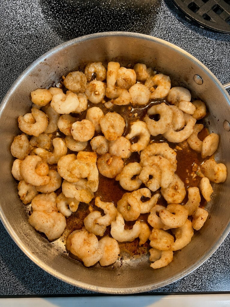 Shrimp sautéing with seasoning and garlic in a skillet for parmesan steak and shrimp.