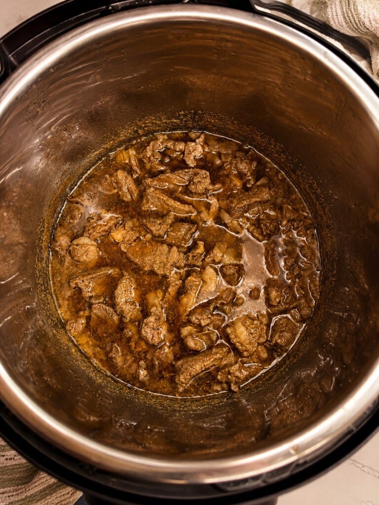 Tender beef cooking in a rich soy sauce and beef broth mixture inside the Instant Pot pressure cooker.