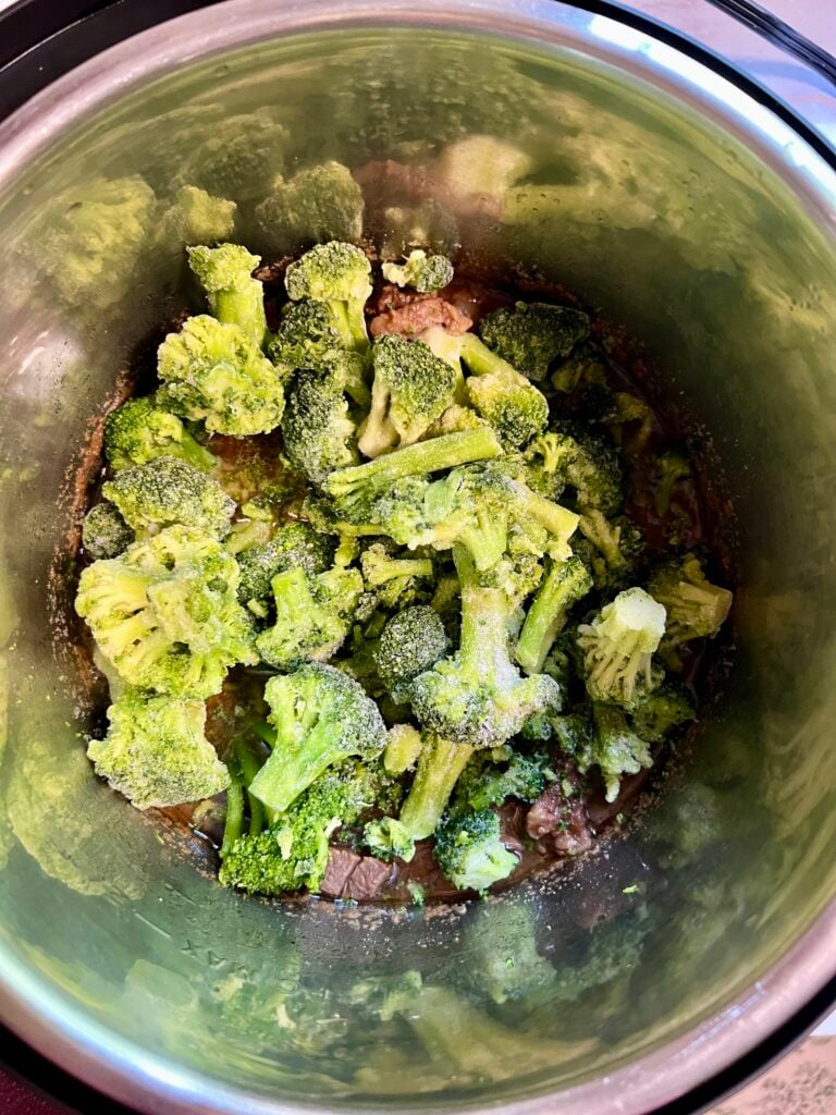 Frozen broccoli added to cooked beef and savory sauce in the Instant Pot for homemade beef and broccoli recipe.