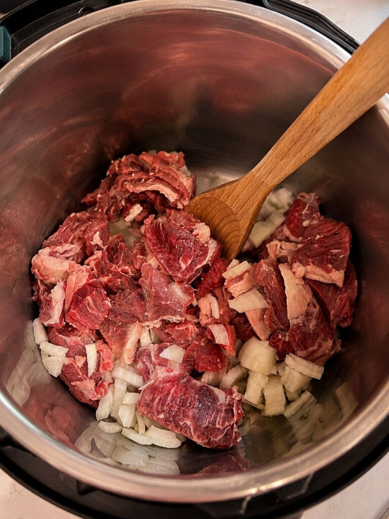 Raw steak and chopped onions sautéing inside an Instant Pot before pressure cooking for homemade beef and broccoli recipe.