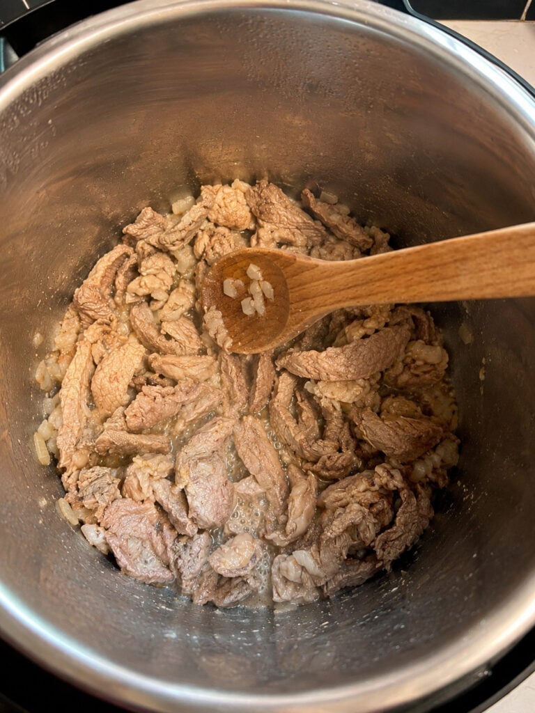 Thinly sliced beef and onions browning in the Instant Pot during the first step of making beef and broccoli.