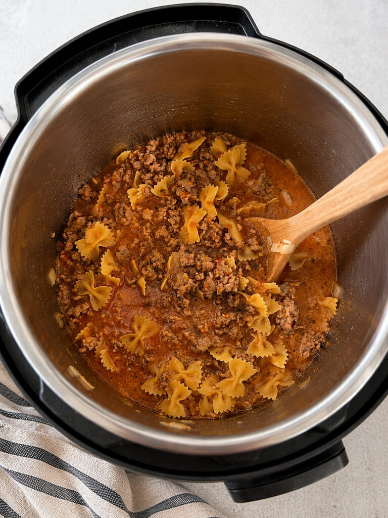 Farfalle pasta added to seasoned meat sauce in an Instant Pot before pressure cooking
