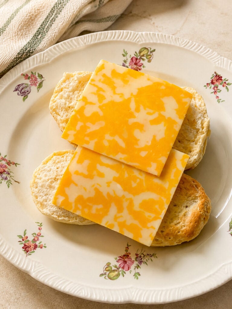 Open biscuit layered with marbled cheese slices and crispy hash browns for a breakfast biscuit sandwich.