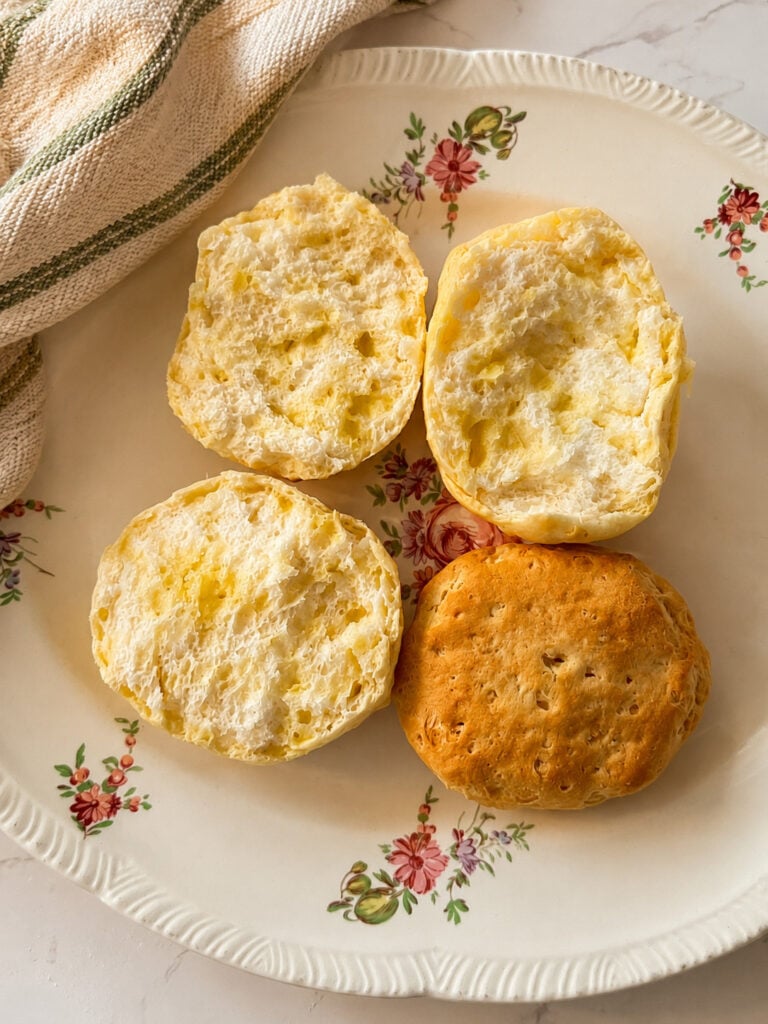 Fluffy homemade biscuit split open to show soft buttery texture beside a golden brown baked biscuit on a floral plate.