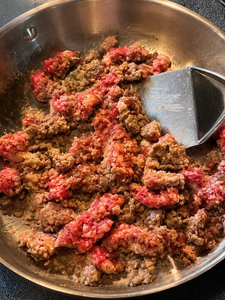 Ground breakfast sausage cooking in a stainless steel skillet on the stovetop for homemade sausage gravy.