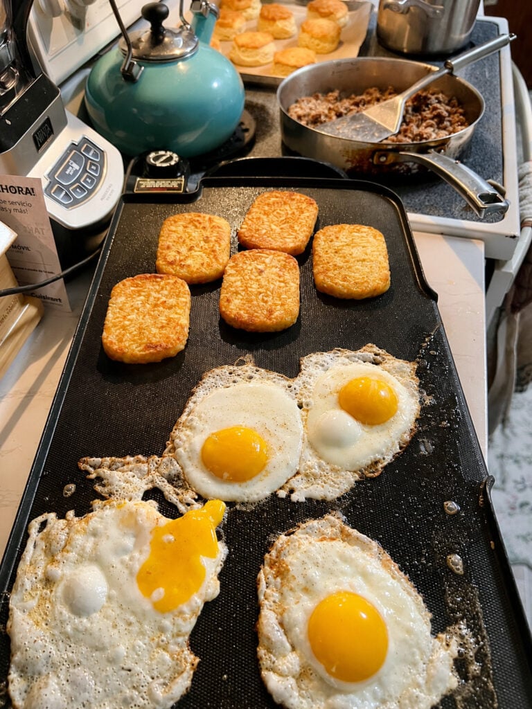 Breakfast griddle with crispy hash browns, sunny side up eggs, sausage skillet, and fresh biscuits for a loaded biscuits and gravy breakfast.